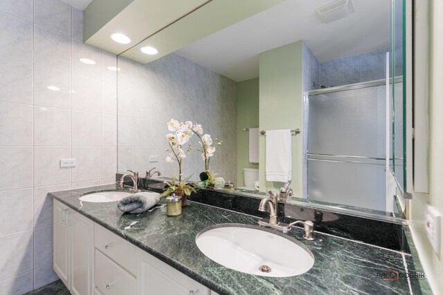 bathroom with tile walls, toilet, visible vents, and a sink