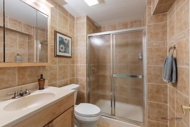 bathroom featuring toilet, tile walls, a stall shower, and vanity