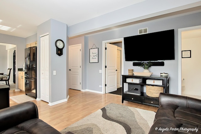 living room featuring visible vents, light wood-style flooring, and baseboards