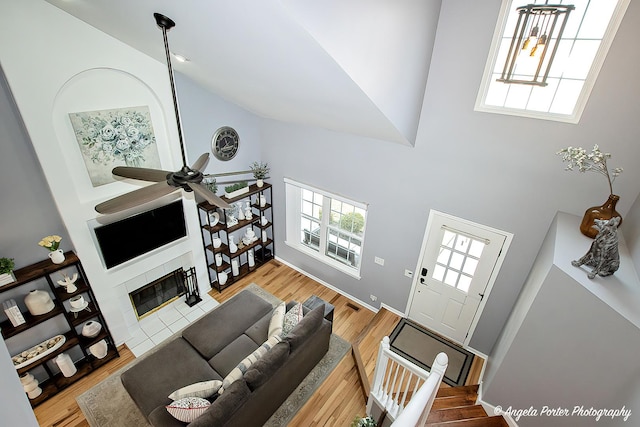 living area with high vaulted ceiling, wood finished floors, visible vents, a ceiling fan, and a tiled fireplace