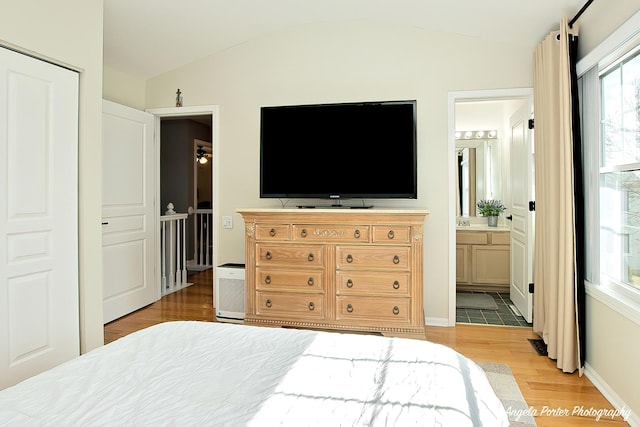 bedroom featuring vaulted ceiling, light wood finished floors, connected bathroom, and baseboards