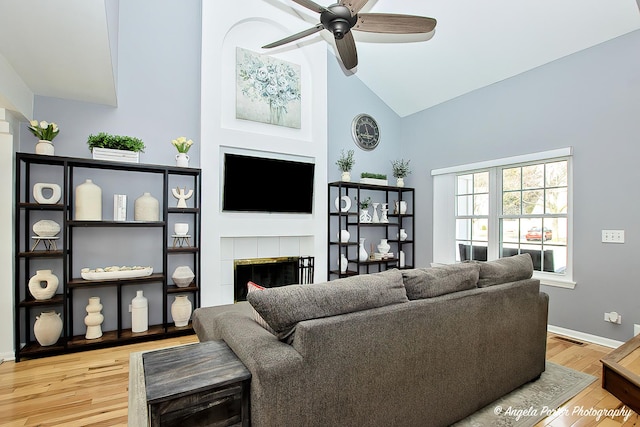 living room featuring light wood finished floors, visible vents, a tiled fireplace, ceiling fan, and high vaulted ceiling