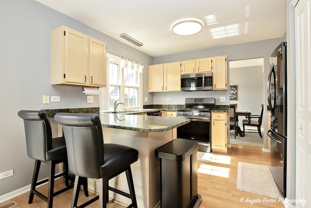 kitchen with stainless steel appliances, a sink, light wood-type flooring, a peninsula, and a kitchen breakfast bar