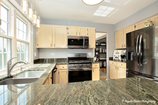 kitchen with dark stone counters, a sink, black appliances, and light brown cabinetry