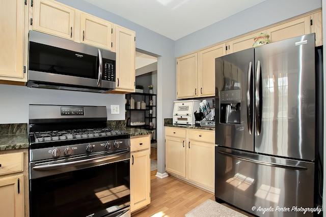 kitchen featuring light wood-type flooring, dark stone countertops, stainless steel appliances, and cream cabinetry