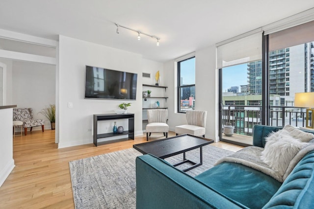 living area featuring visible vents, baseboards, light wood-style floors, a wall of windows, and track lighting