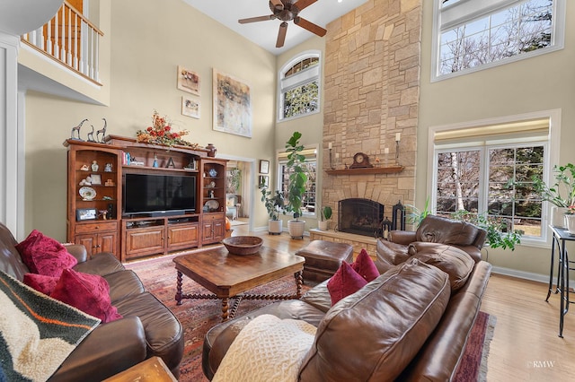 living area featuring a ceiling fan, baseboards, a high ceiling, a fireplace, and light wood-type flooring