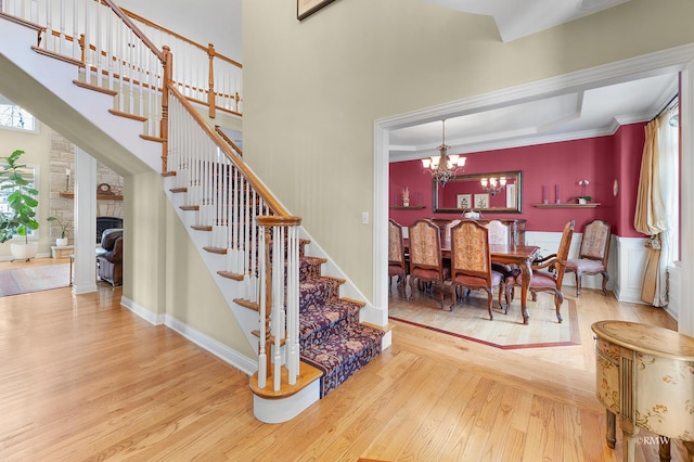 stairway featuring wood finished floors, a towering ceiling, a stone fireplace, crown molding, and a chandelier