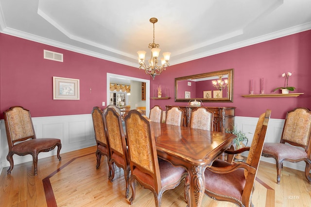 dining space featuring visible vents, a wainscoted wall, an inviting chandelier, light wood finished floors, and a raised ceiling