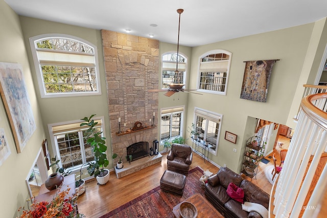 living room featuring ceiling fan, a fireplace, a towering ceiling, and wood finished floors