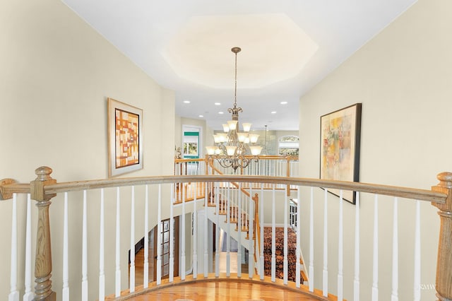 stairs featuring recessed lighting, a raised ceiling, an inviting chandelier, and wood finished floors