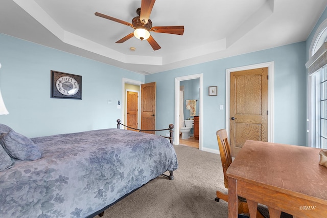 carpeted bedroom with a tray ceiling, baseboards, ensuite bath, and ceiling fan