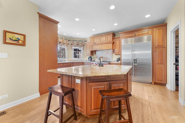 kitchen featuring light stone counters, light wood finished floors, a breakfast bar, stainless steel built in fridge, and tasteful backsplash