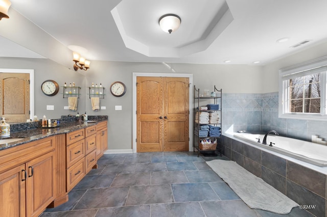 full bathroom featuring visible vents, a sink, double vanity, a raised ceiling, and a bath