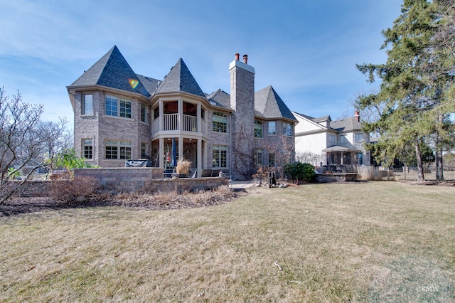 rear view of property featuring a balcony, a yard, brick siding, a chimney, and a patio area