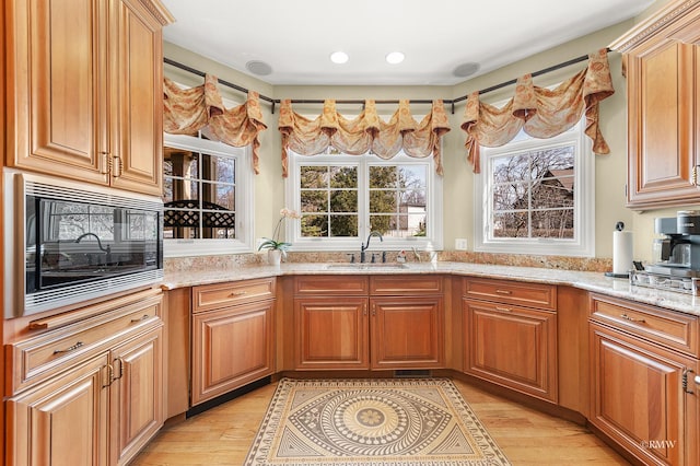 kitchen with built in microwave, light stone counters, recessed lighting, light wood-style flooring, and a sink