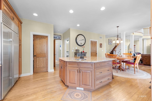 kitchen with a kitchen island, built in refrigerator, light stone counters, recessed lighting, and light wood-style floors