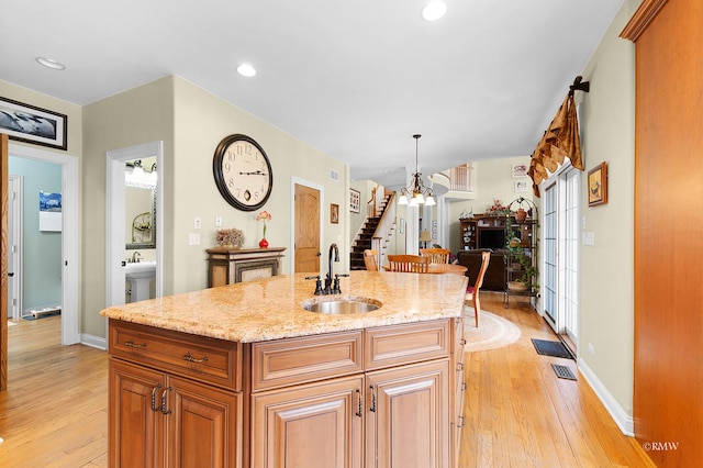 kitchen with a sink, a notable chandelier, light stone counters, and light wood-style floors