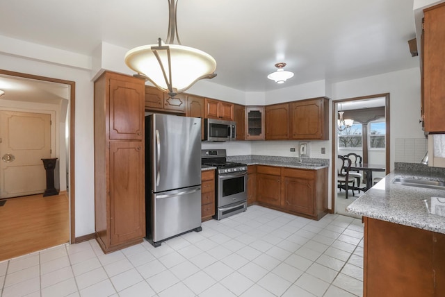 kitchen with light stone counters, a sink, appliances with stainless steel finishes, decorative backsplash, and brown cabinetry