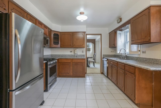 kitchen featuring stainless steel appliances, brown cabinetry, a sink, and backsplash