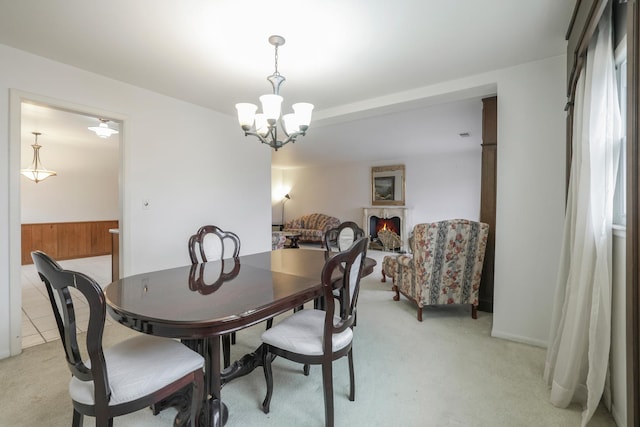 dining room featuring a warm lit fireplace, wainscoting, a notable chandelier, and light colored carpet