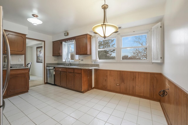 kitchen featuring wooden walls, a wainscoted wall, stainless steel appliances, a sink, and brown cabinetry