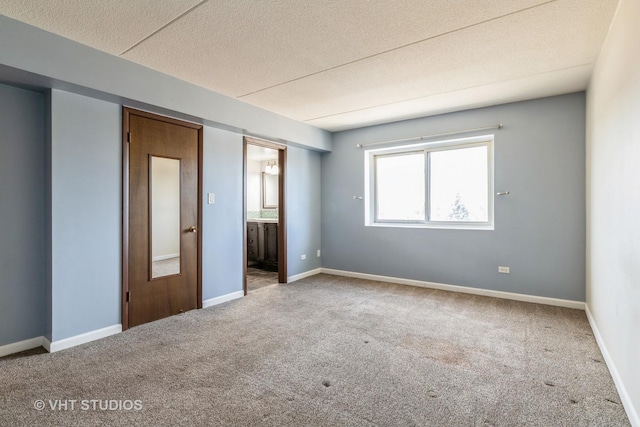 unfurnished bedroom with baseboards, carpet, ensuite bathroom, and a textured ceiling