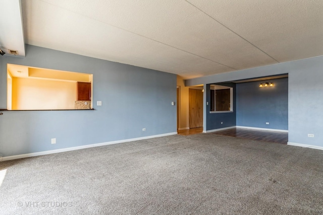 unfurnished room featuring baseboards, dark carpet, and a textured ceiling