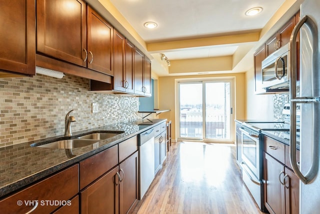 kitchen featuring a sink, backsplash, light wood-style floors, appliances with stainless steel finishes, and a raised ceiling