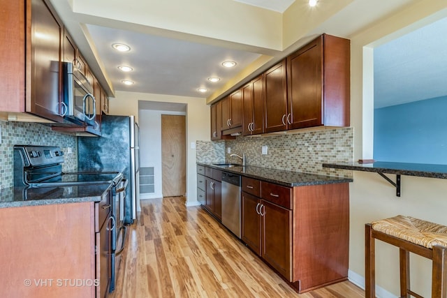 kitchen with dark stone countertops, baseboards, a sink, stainless steel appliances, and light wood-style floors