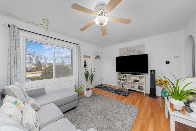 living area with light wood-style floors, arched walkways, and a ceiling fan