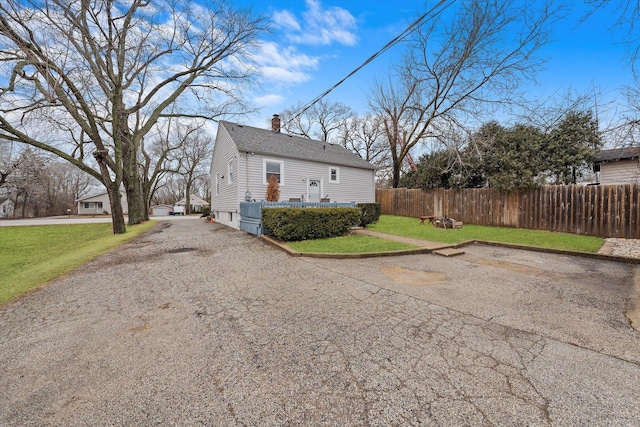 view of side of home featuring roof with shingles, a chimney, fence, and a yard