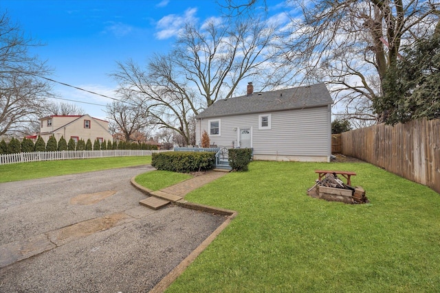 rear view of property featuring an outdoor fire pit, fence private yard, a shingled roof, a yard, and a chimney