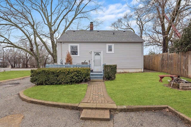 view of front of house with roof with shingles, a chimney, a front yard, and fence