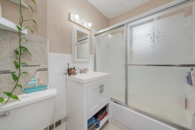 full bathroom featuring vanity, tile walls, toilet, and bath / shower combo with glass door