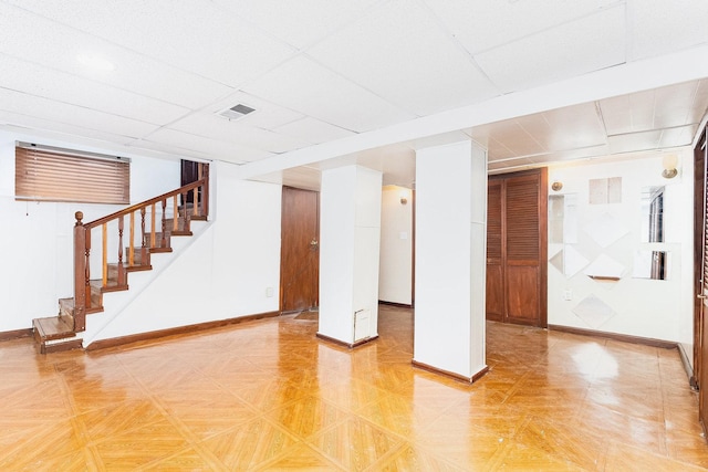 finished below grade area with stairs, visible vents, a paneled ceiling, and baseboards