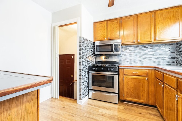 kitchen featuring brown cabinets, light wood-style flooring, stainless steel appliances, and backsplash