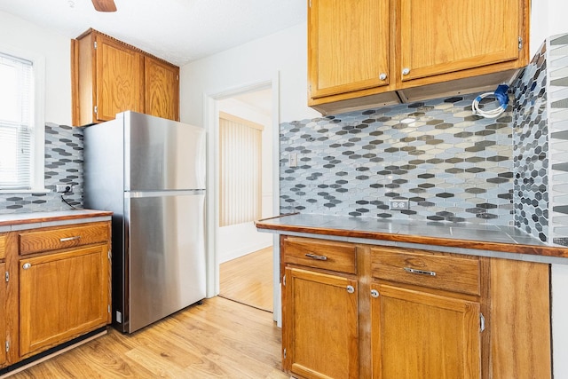 kitchen featuring tile countertops, decorative backsplash, freestanding refrigerator, and light wood-style floors