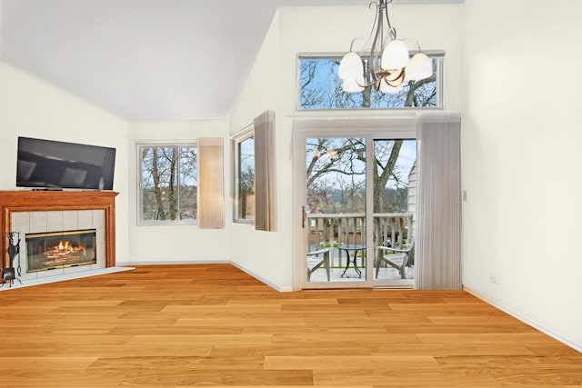 interior space with baseboards, a tiled fireplace, lofted ceiling, light wood-style flooring, and a chandelier