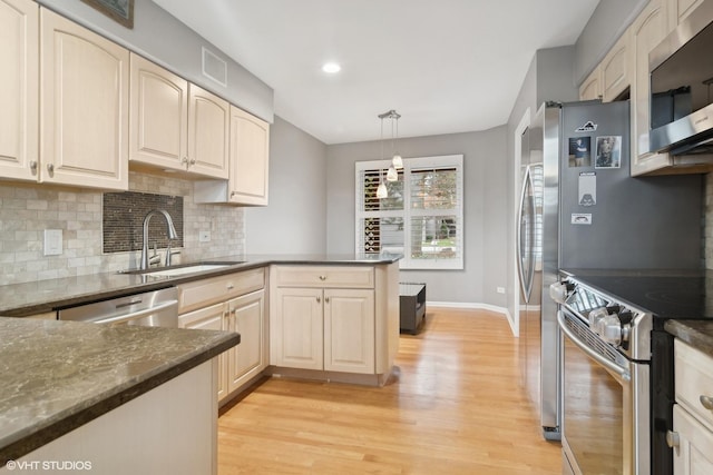 kitchen featuring stainless steel appliances, a peninsula, a sink, backsplash, and light wood finished floors