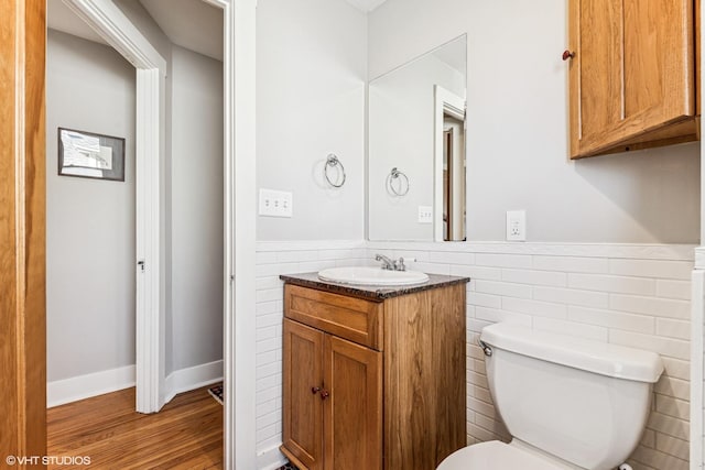 half bathroom with a wainscoted wall, toilet, vanity, and wood finished floors