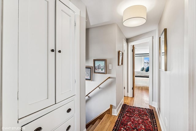 corridor featuring baseboards, an upstairs landing, and light wood finished floors