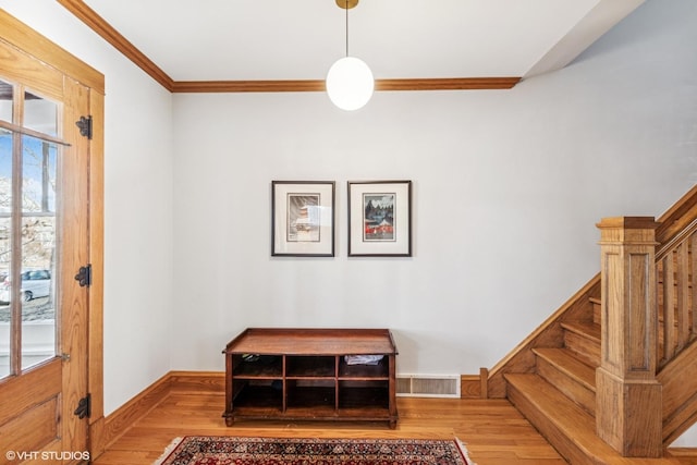 entryway with wood finished floors, visible vents, baseboards, stairs, and crown molding