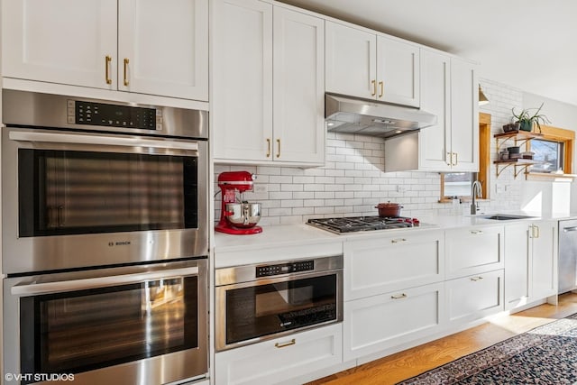 kitchen featuring a sink, light countertops, appliances with stainless steel finishes, under cabinet range hood, and white cabinetry