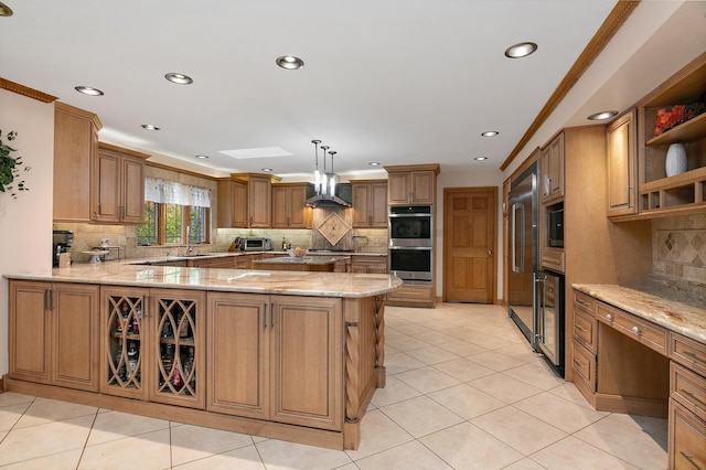 kitchen featuring light tile patterned floors, brown cabinetry, wall chimney range hood, light stone countertops, and built in appliances