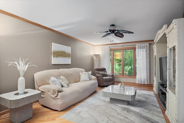 living room featuring light wood-style flooring, a ceiling fan, and crown molding