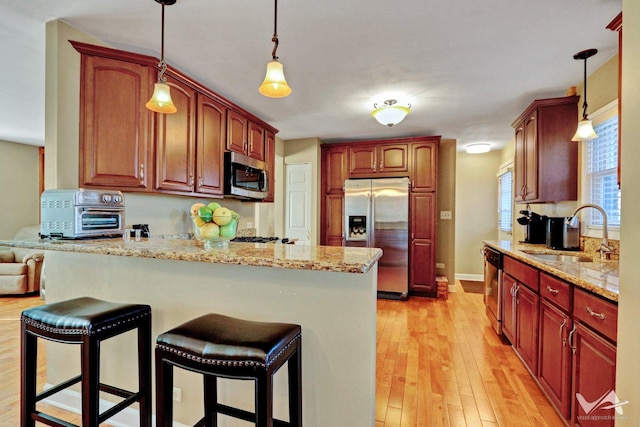 kitchen with stainless steel appliances, a peninsula, a sink, a kitchen breakfast bar, and light wood-style floors