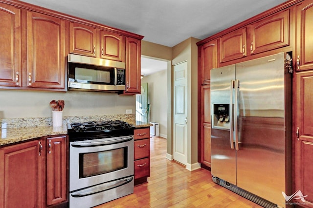 kitchen featuring light stone countertops, light wood-style flooring, appliances with stainless steel finishes, and baseboards