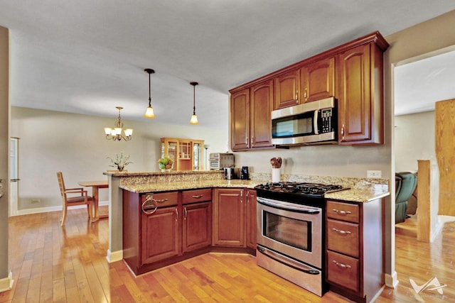 kitchen with light wood-style flooring, a peninsula, appliances with stainless steel finishes, light stone countertops, and decorative light fixtures