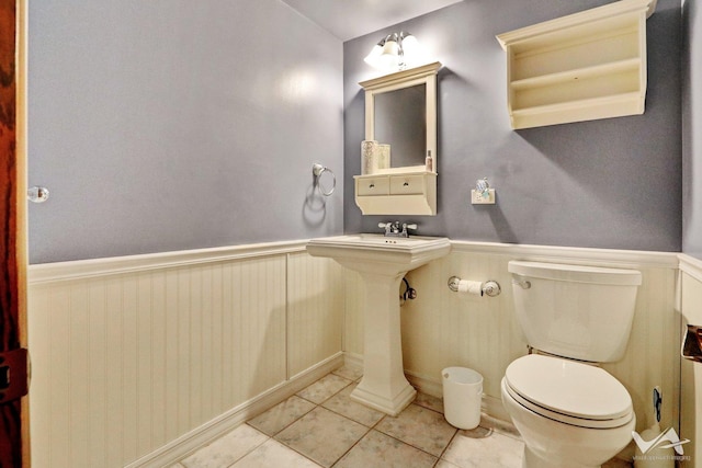 half bathroom featuring toilet, a wainscoted wall, and tile patterned flooring